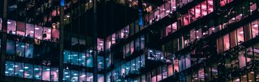 View of an office building with blue and pink lights illuminating the night sky.