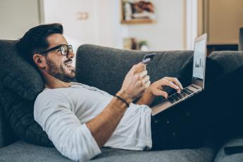 Man holding card while typing on laptop and smiling.
