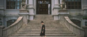Man walking in front of official building looking at his mobile