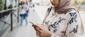 woman outside wearing hijab looking at her mobile phone
