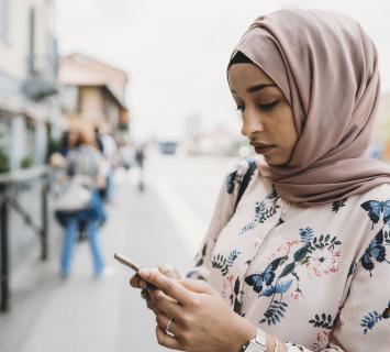 woman outside wearing hijab looking at her mobile phone